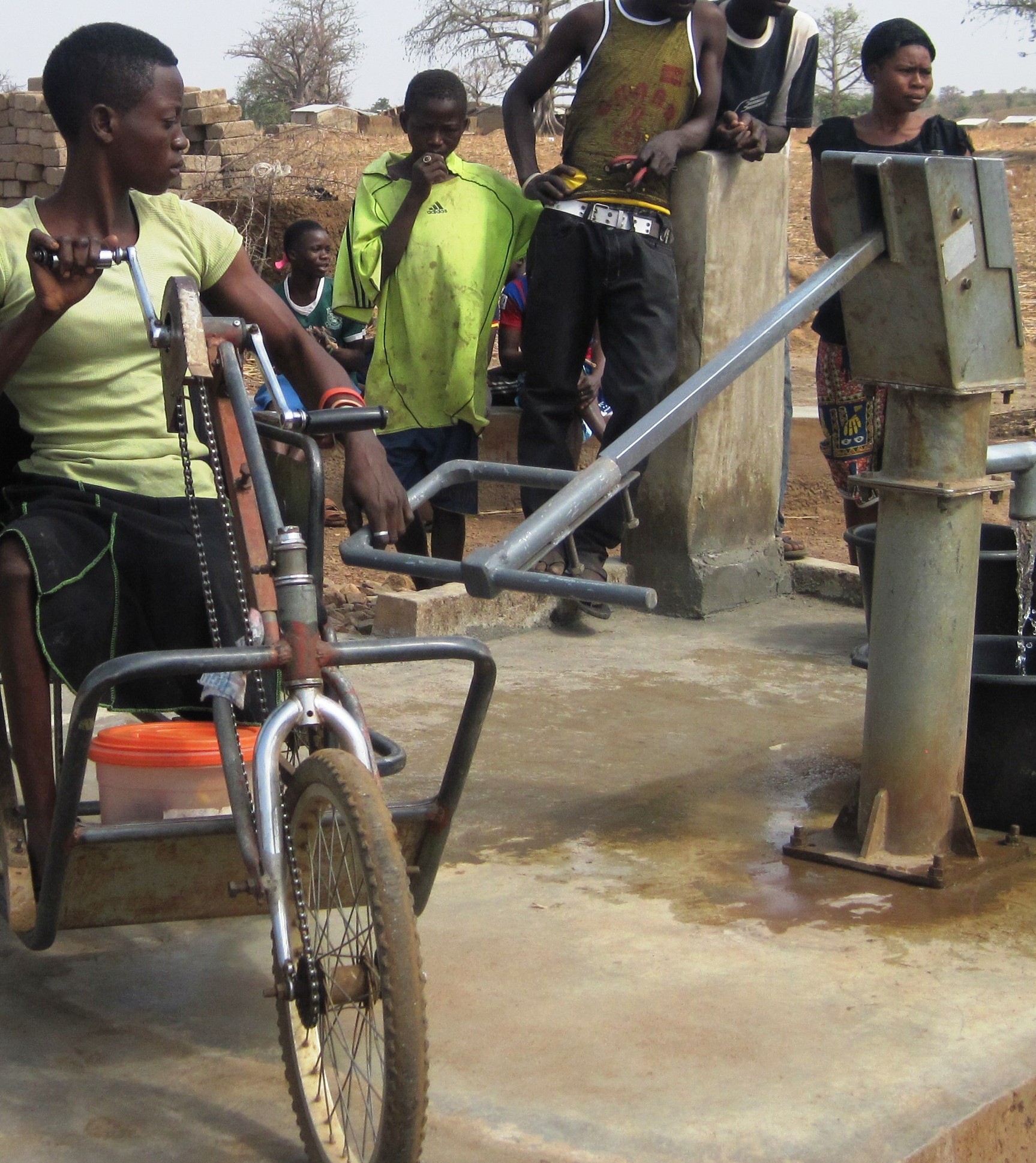 A woman using a tricycle operates a lengthened pump handle 