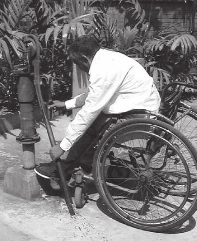 A man using a wheelchair is handling a handpump placed at 90 degrees to the height of the wheelchair