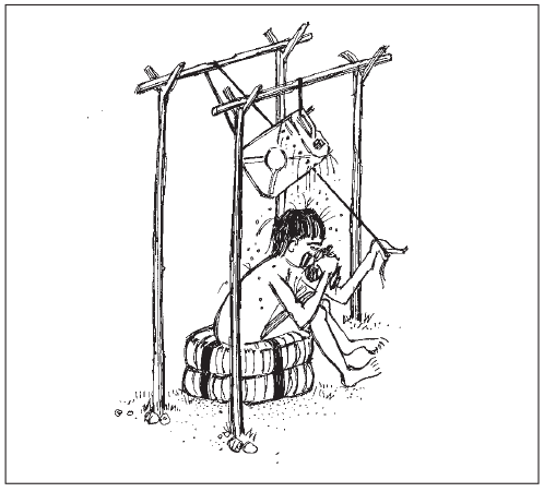 Seorang anak laki-laki duduk di atas dua ban, menggunakan sistem pancuran di mana jerigen digantung di 4 tiang dan diatur menggunakan tali.