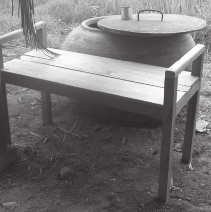 A bathing bench in wood in front of a jar of water for washing