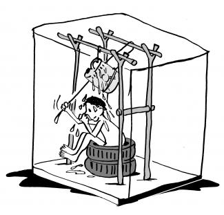 A boy sitting on two tyres, using a shower system where a jerrycan has been hanged across 4 poles and managed through a rope